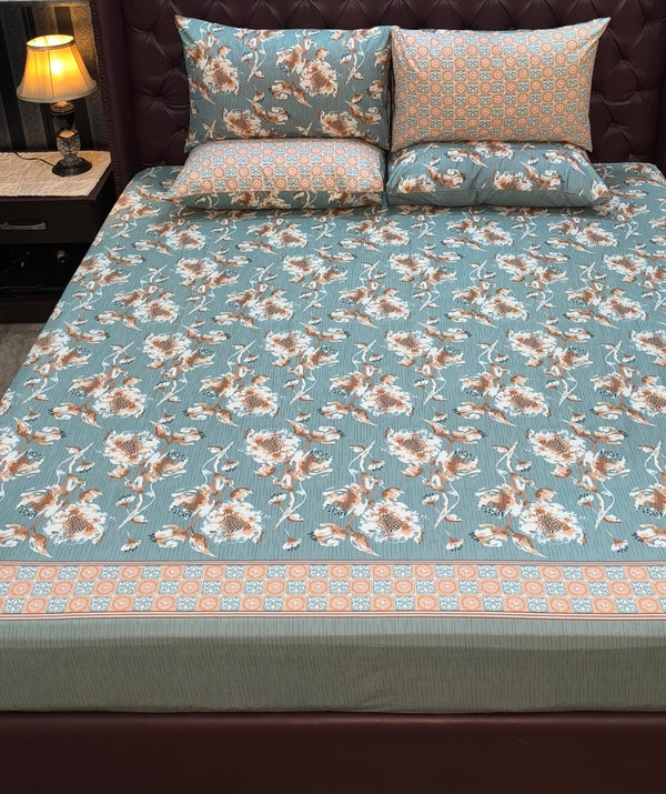 Floral patterned bedspread on a bed with matching pillows, nightstand with lamp in the background.